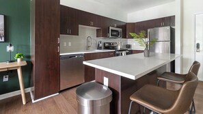 Een moderne keuken met donkere houtkasten, roestvrijstalen apparatuur, een wit aanrechtblad en een prullenbak.