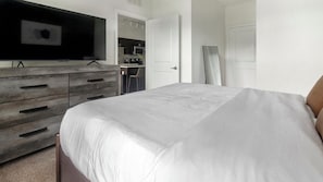 A bedroom with a bed, a dresser, a television, and a door leading to a kitchenette. - Landing | Stylish 1BD, Gym, Clubhouse (Jacksonville)