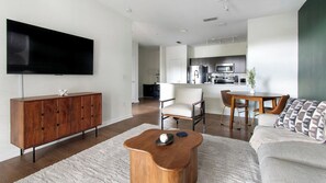 A modern living room with a flat-screen TV, wooden cabinet, and a round coffee table. - Landing | Stunning 1BD, Clubhouse, Gym (Jacksonville)
