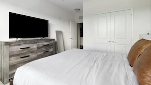 Ein Schlafzimmer mit Bett, Kommode, Fernseher und Kleiderschrank.