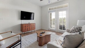Ein modernes Wohnzimmer mit Flachbildfernseher, Holzschrank und einer Couch mit gemusterten Kissen.