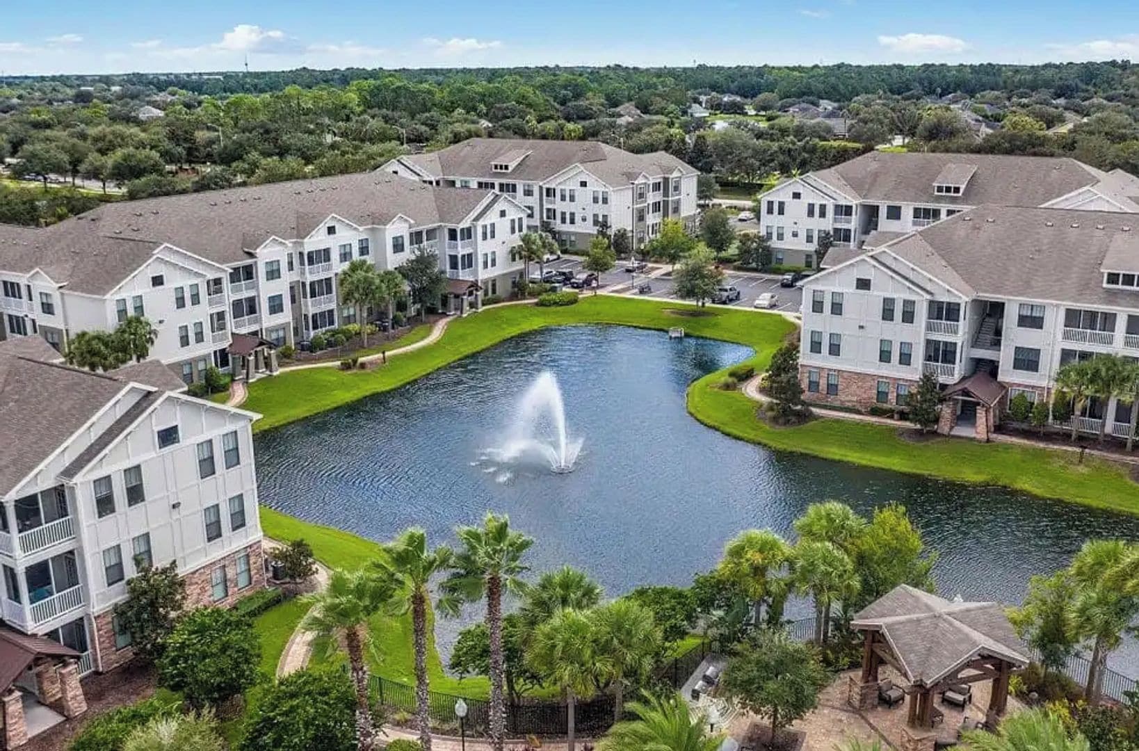 A residential area with modern apartment buildings, a central pond with a fountain, and well-maintained green spaces.