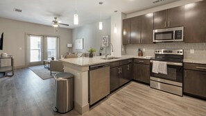 A modern kitchen with stainless steel appliances, a central island, and a dining area with a view. - Landing | Incredible 1BD, Rooftop Lounge (Fort Worth)