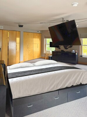 A bedroom with a large bed, a television mounted on the wall, and a wardrobe. - Historic 1868 Loft Sleeps 10 - Downtown State St (Rockford)