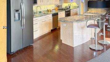 A modern kitchen with stainless steel appliances, wooden cabinets, and a bar area with stools.