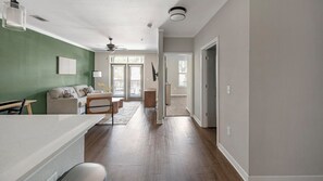 A modern interior with a kitchen area, a living room with a sofa and coffee table, and a hallway leading to another room. - Landing | Modern 1BD, Gym (Bluffton)