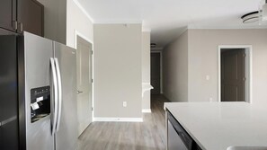 A modern kitchen with stainless steel appliances, a white countertop, and a wooden floor. - Landing | Stunning 1BD, Gym (Bluffton)