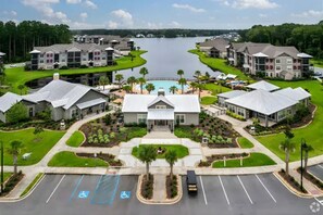 A residential area with a central building, a parking lot with handicapped spaces, and a body of water in the background. - Landing | Stunning 1BD, Gym (Bluffton)