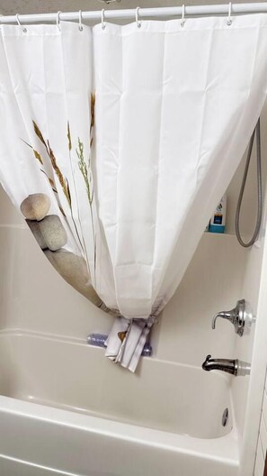 Una bañera con cortina blanca decorada con motivos naturales, una manguera de ducha y un perchero con toallas.