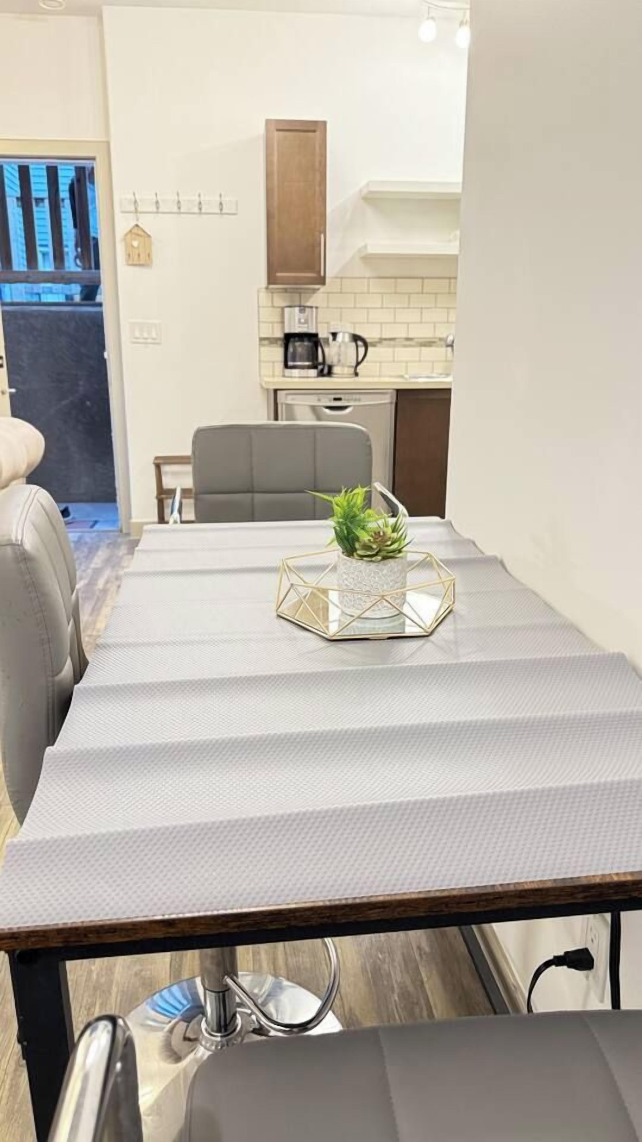 A dining table with a geometric centerpiece, a kitchen area with a coffee maker, and a view of the outside.