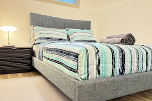 Una cama bien hecha con ropa de cama a rayas, una mesita de noche con lámpara y una toalla enrollada en el suelo.