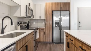 Une cuisine moderne équipée d’appareils électroménagers en acier inoxydable, de meubles en bois et d’un réfrigérateur encastré.