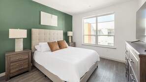 A bedroom with a large bed, two bedside tables with lamps, a dresser, and a window with a view of buildings. - Landing | Spectacular 2BD, Gym (Phoenix)