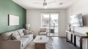 A modern living room with a sofa, coffee table, and a TV mounted on the wall. - Landing | Spectacular 2BD, Gym (Phoenix)