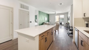 A modern kitchen with a central island, wooden cabinets, and a dining area with a table and chairs. - Landing | Spectacular 2BD, Gym (Phoenix)