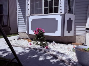 A house with a white exterior, a small garden with white gravel, and a pink flowering plant. - The Crossing Haven | 3BR Home (Calgary)