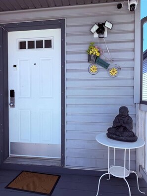 A white door with a small window, a security camera above it, a welcome sign, and a statue on a small table. - The Crossing Haven | 3BR Home (Calgary)