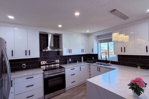 Cozinha moderna com armários brancos, painel de fundo preto, eletrodomésticos de aço inoxidável e bancada de mármore.