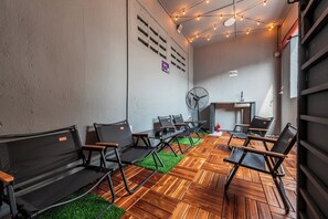 A room with a herringbone wooden floor, black foldable chairs, a table, a fan, and string lights.