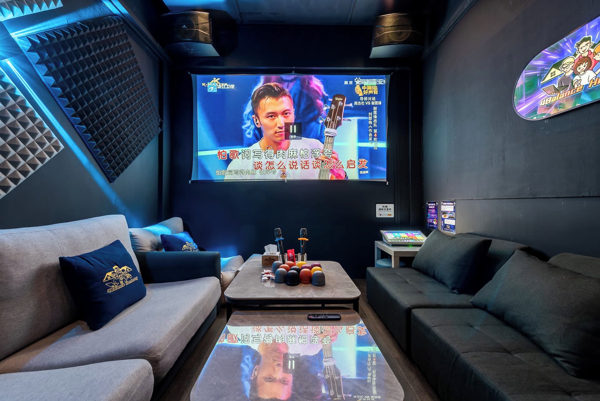 A modern lounge area with a large screen displaying a program, comfortable seating, and a small table with a remote control.