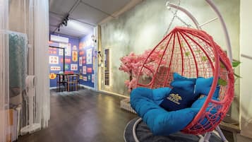 A room with a hanging chair, a desk with chairs, and a wall with various stickers.
