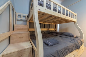 A bunk bed with a wooden frame, a desk with drawers, and a window.