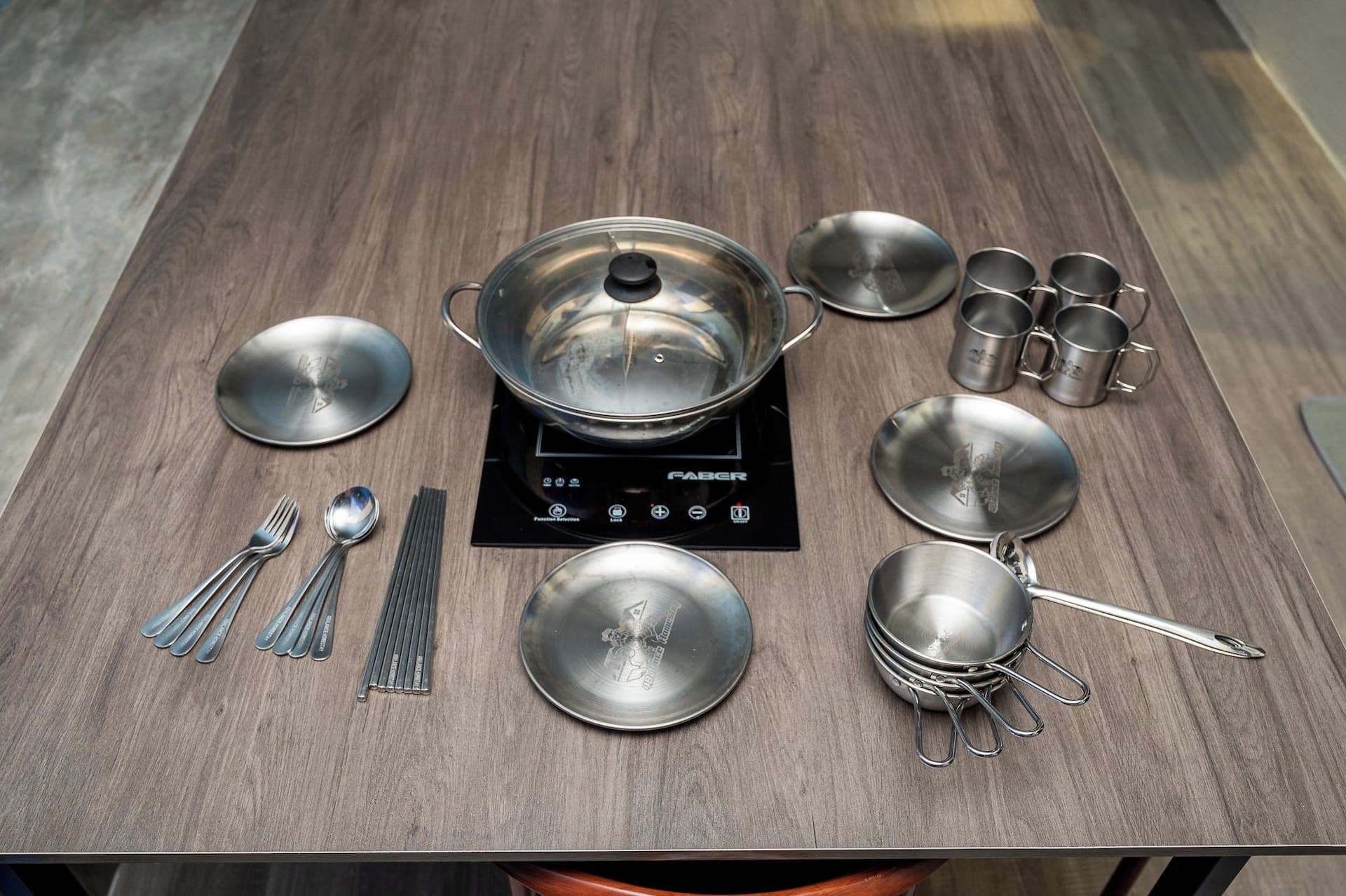 A table with a portable electric stove, various metal cookware, and utensils.