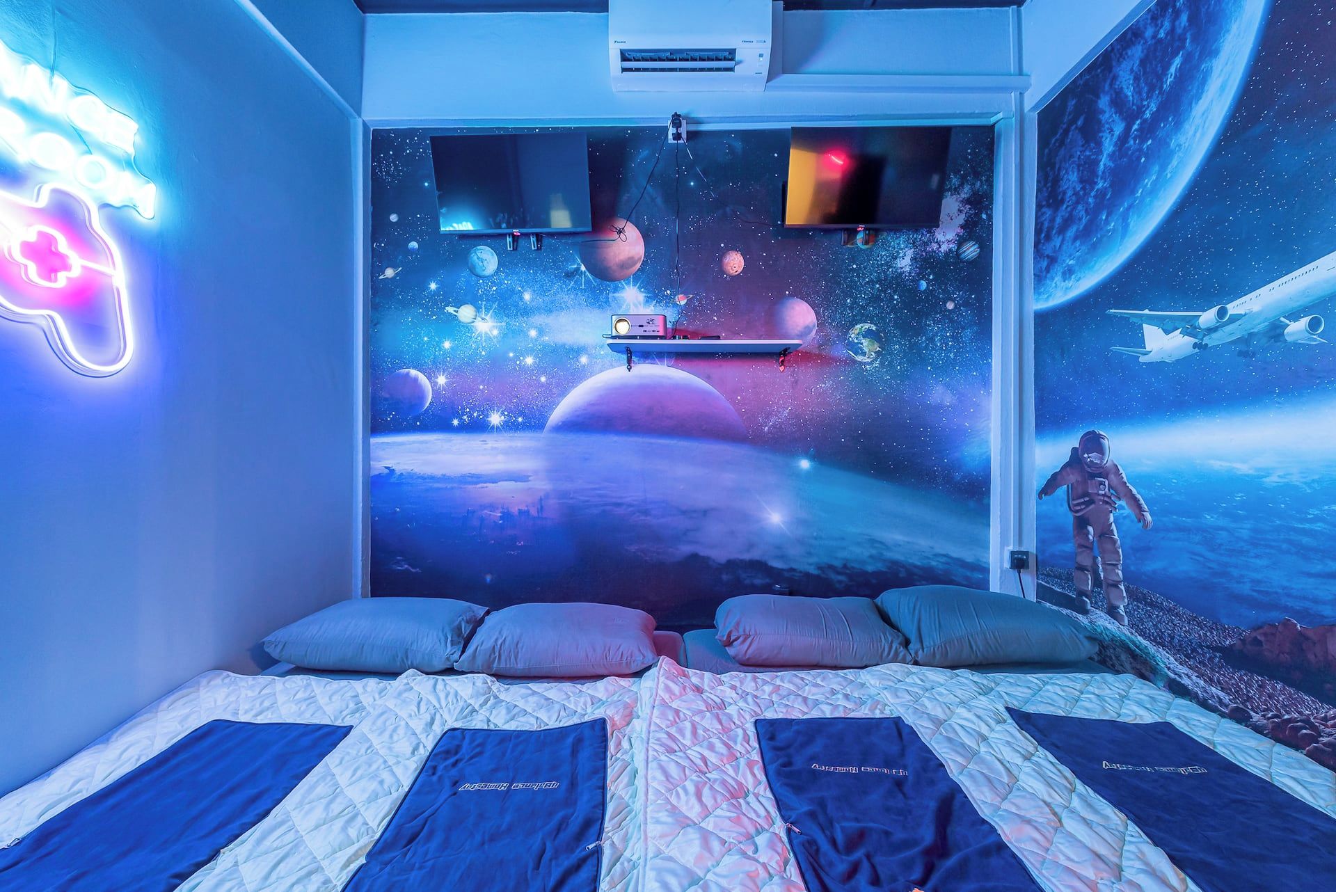 Una camera da letto con un murale a tema spaziale, un letto con numerosi cuscini e un'insegna luminosa al neon.