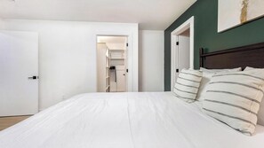 Une chambre avec un grand lit, une literie blanche, une tête de lit sombre et un mur d’accent vert.