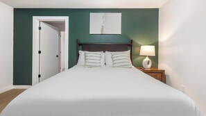 A bedroom with a bed, a nightstand, a lamp, and a door. - Landing | Chic 1BD, Gym (Bridgeport)