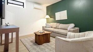 A modern living room with a sofa, a coffee table, and a TV on a stand. - Landing | Beautiful 1BD, Gym (Bridgeport)