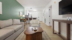 A living room with a sofa, a wooden coffee table, and a television on a stand. - Landing | Beautiful 1BD, Gym (Bridgeport)