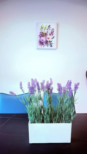 A white rectangular planter with lavender plants on a dark floor, a blue wall, and a framed floral artwork above. - Savanna Breeze | Modern 3BR | Near YYC Airport (Calgary)