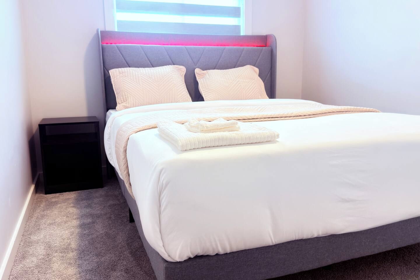 A neatly made bed with a grey headboard, two pillows, and a folded blanket.