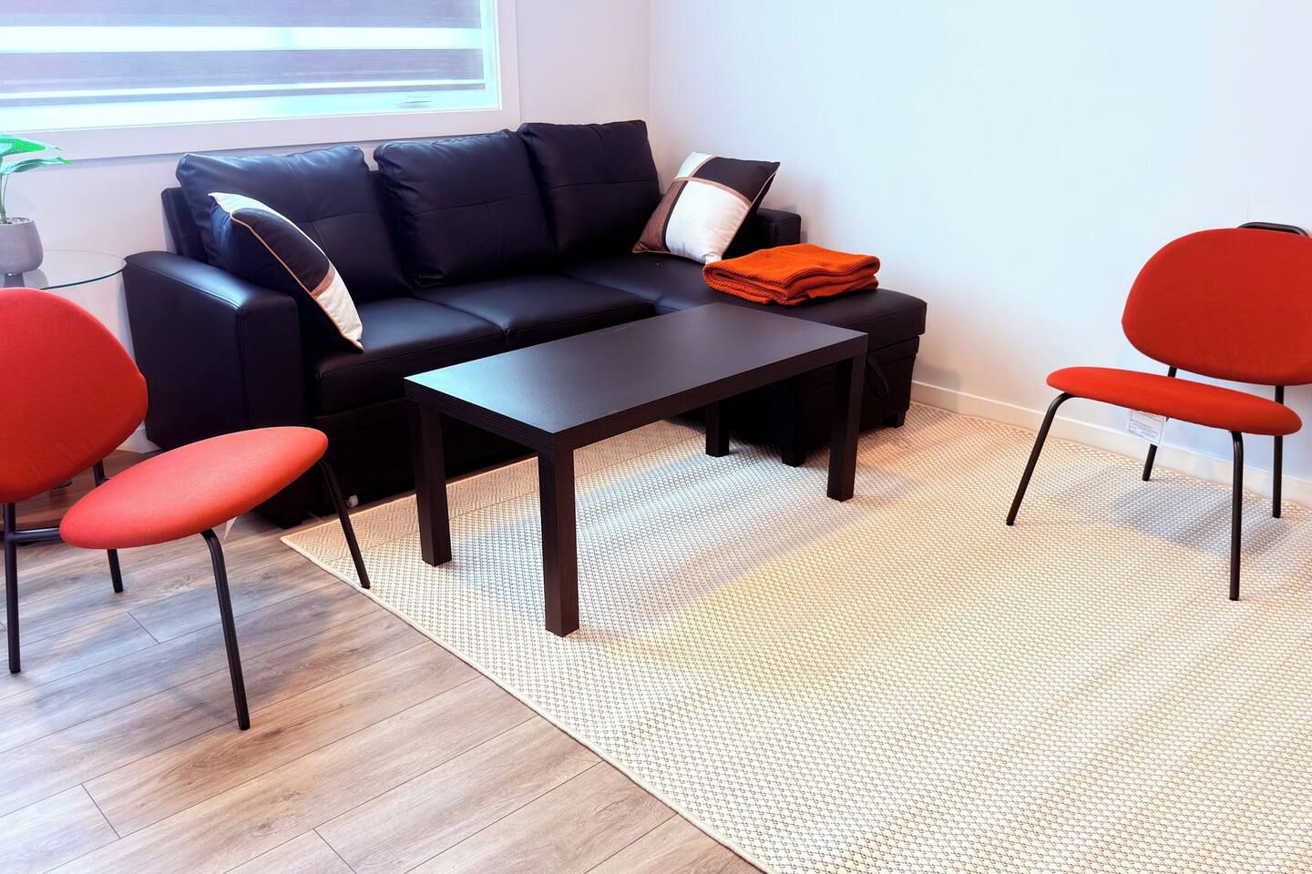 A modern living room with a black sofa, two red chairs, a dark coffee table, and a patterned rug.