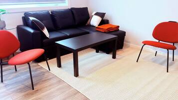 A modern living room with a black sofa, two red chairs, a dark coffee table, and a patterned rug.