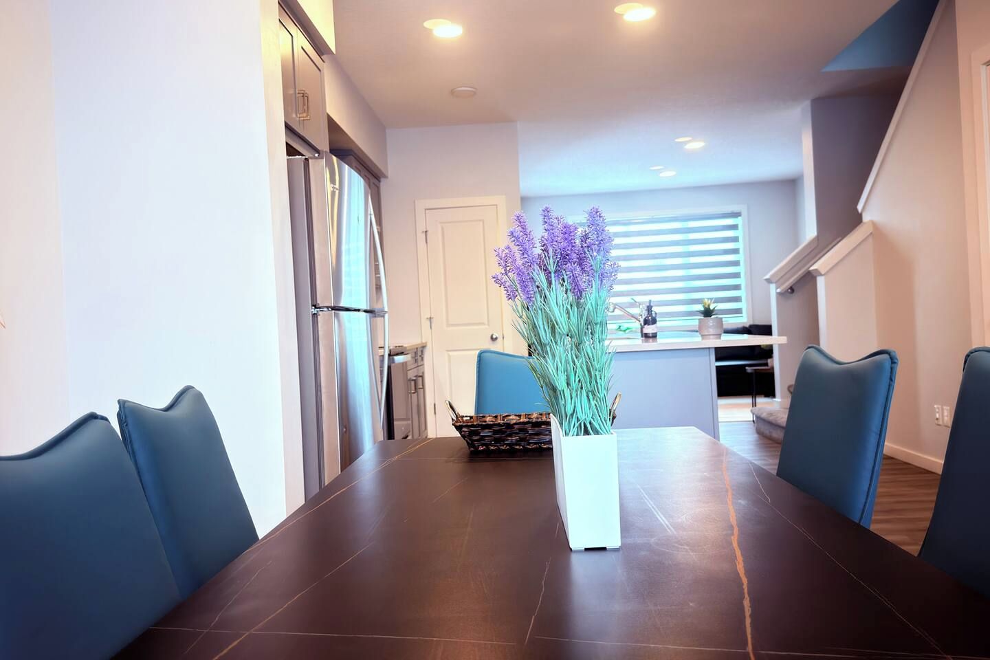 A modern dining area with a dark wooden table, blue chairs, and a vase of purple flowers.