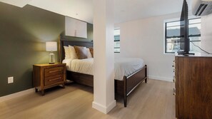 A bedroom with a bed, bedside table, lamp, and a TV on a stand. - Landing | Spectacular 2BD, Gym (Bridgeport)