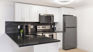 Une cuisine moderne avec des meubles blancs, un plan de travail noir, des appareils en acier inoxydable et un four encastré.