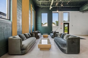 A modern lounge area with sofas and a coffee table, large windows, and a visible door. - Landing | Amazing 2BD, Gym (Bridgeport)