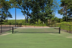 Ein Tennisplatz mit Netz, umgeben von Bäumen und einem Zaun.