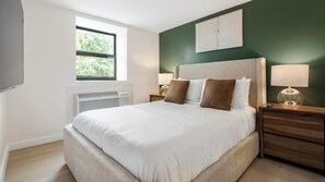 A bedroom with a bed, bedside lamps, a window, and a wall-mounted artwork. - Landing | Stylish 1BD, Gym (Bridgeport)