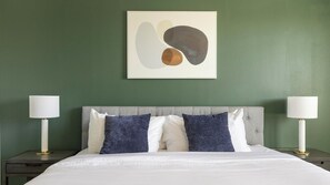 A hotel room with a bed, two bedside lamps, and a wall-mounted abstract painting. - Landing | Spectacular 2BD, Rooftop Lounge (Fort Worth)