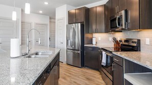 A modern kitchen with stainless steel appliances, granite countertops, and dark wooden cabinets. - Landing | Spectacular 2BD, Rooftop Lounge (Fort Worth)