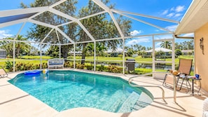A pool area with a covered section, lounge chairs, and a view of a landscaped garden. - Marker Gulf Coast Getaway (Rotonda West)