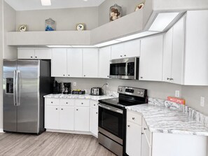 A modern kitchen with white cabinets, stainless steel appliances, a marble countertop, and a welcome sign. - Marker Gulf Coast Getaway (Rotonda West)