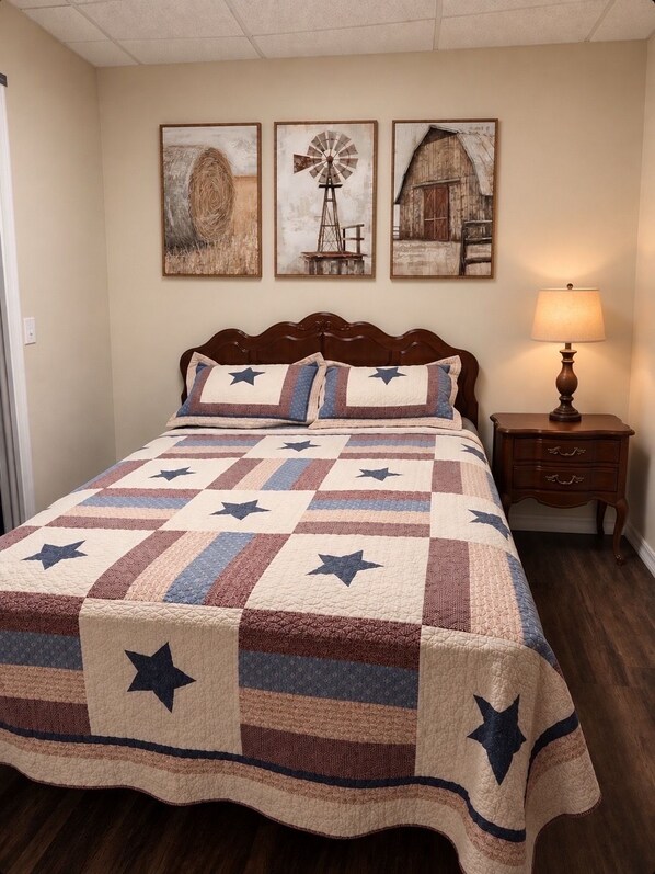 A bedroom with a bed, a nightstand, a lamp, and three wall-mounted paintings.