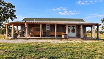 A wooden cabin with a porch, a swing, and a barbecue grill.