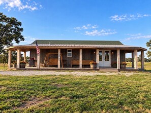 A wooden cabin with a porch, a swing, and a barbecue grill.