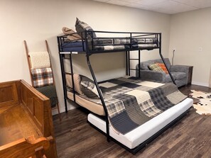 A bunk bed with a quilt, a chair, and a sofa in a room with wooden flooring.